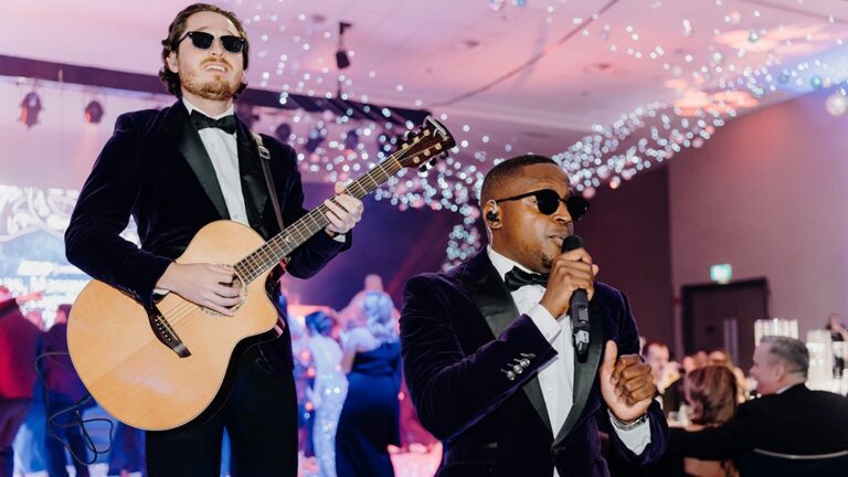 Guitarist and vocalist performing among tables under a fairy-light ceiling, The Function Band