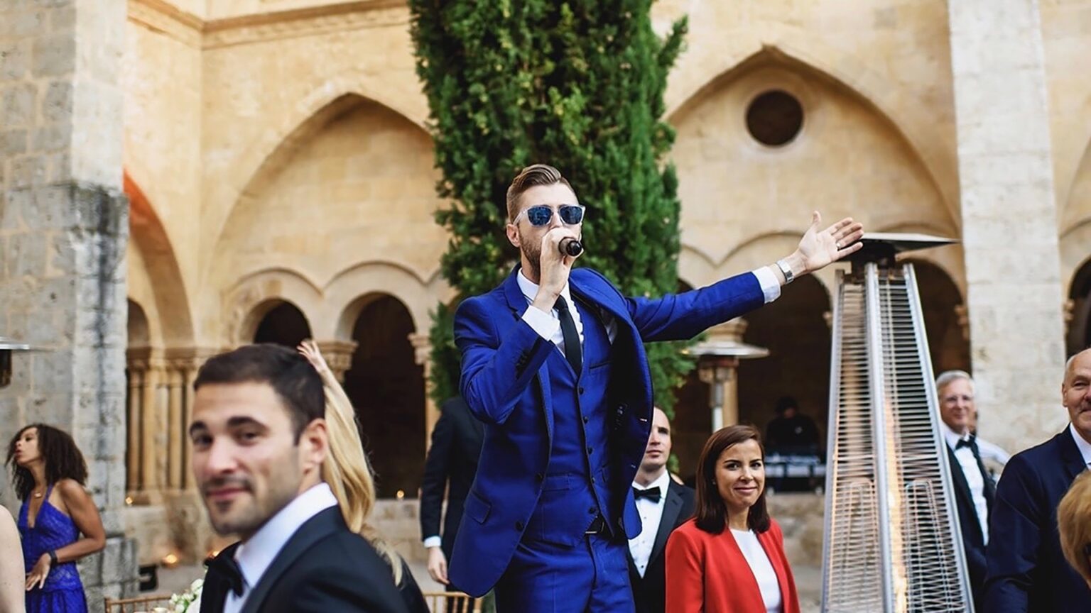 The lead vocalist in a blue suit performing in a stone cloister at a destination wedding