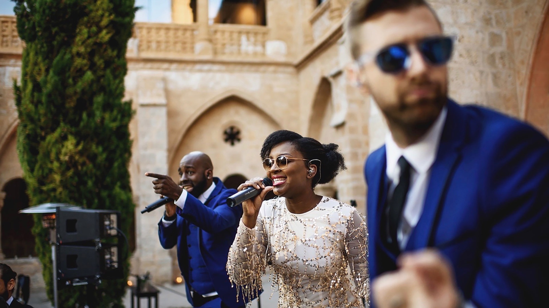 Two vocalists performing to guests in a stone cloister at a destination wedding, The Function Band