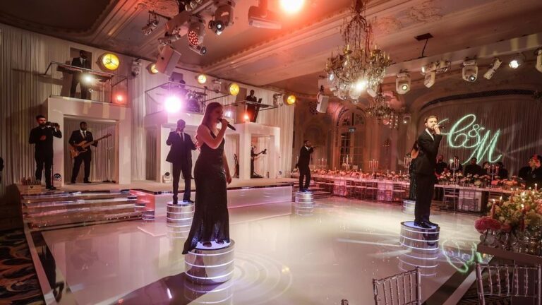Band on raised platforms in a chandeliered ballroom with a monogram projected on the floor, The Function Band