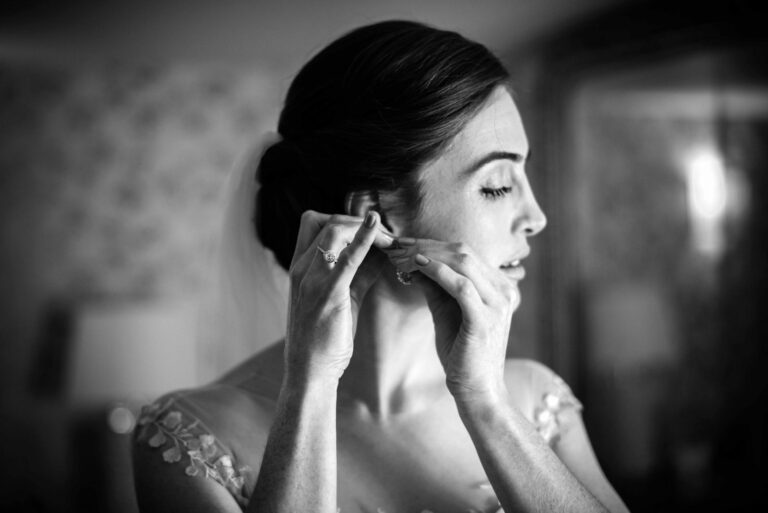The bride fastening her earrings on the morning of the wedding, The George in Rye