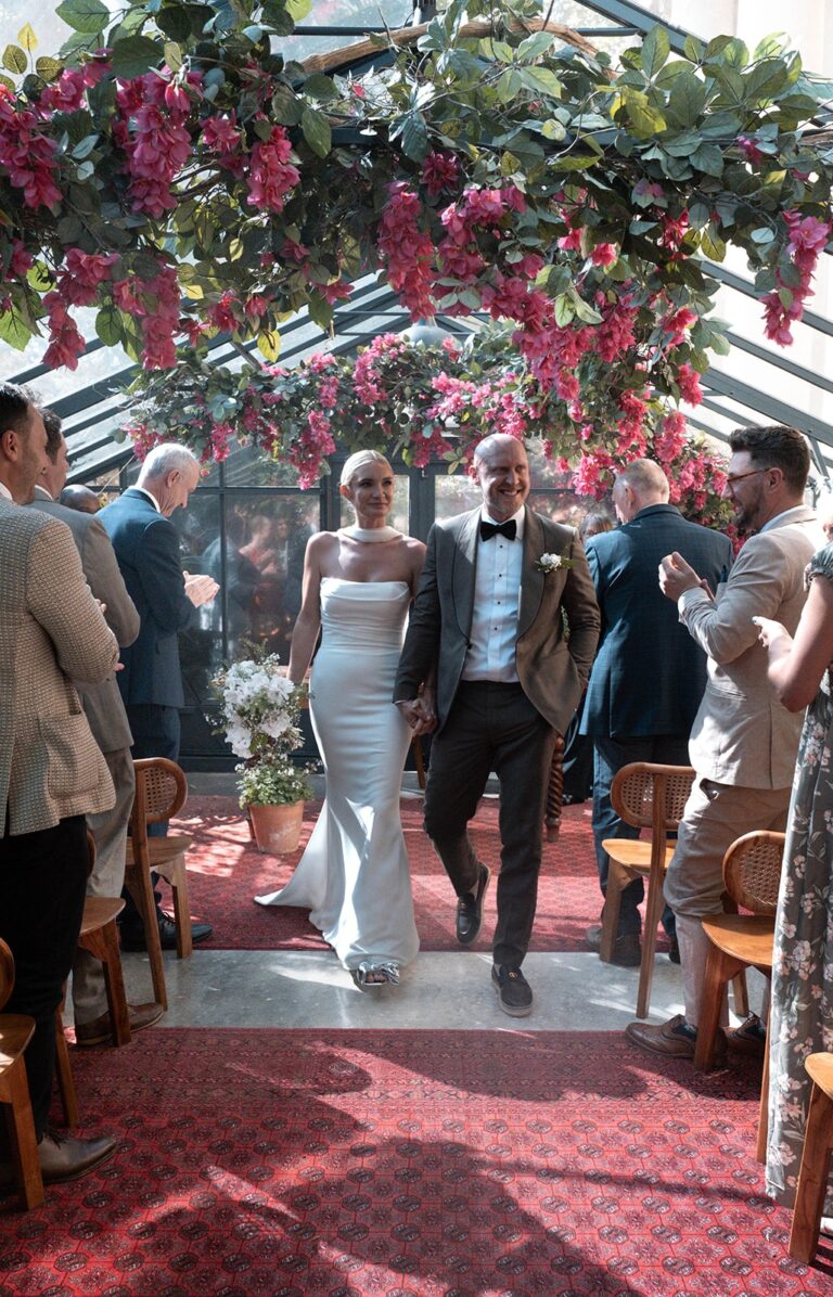 The couple walking back down the aisle between seated guests, The Greenhouses