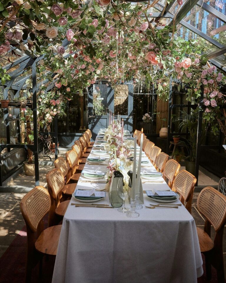 A long dining table beneath a canopy of pink blossom, The Greenhouses