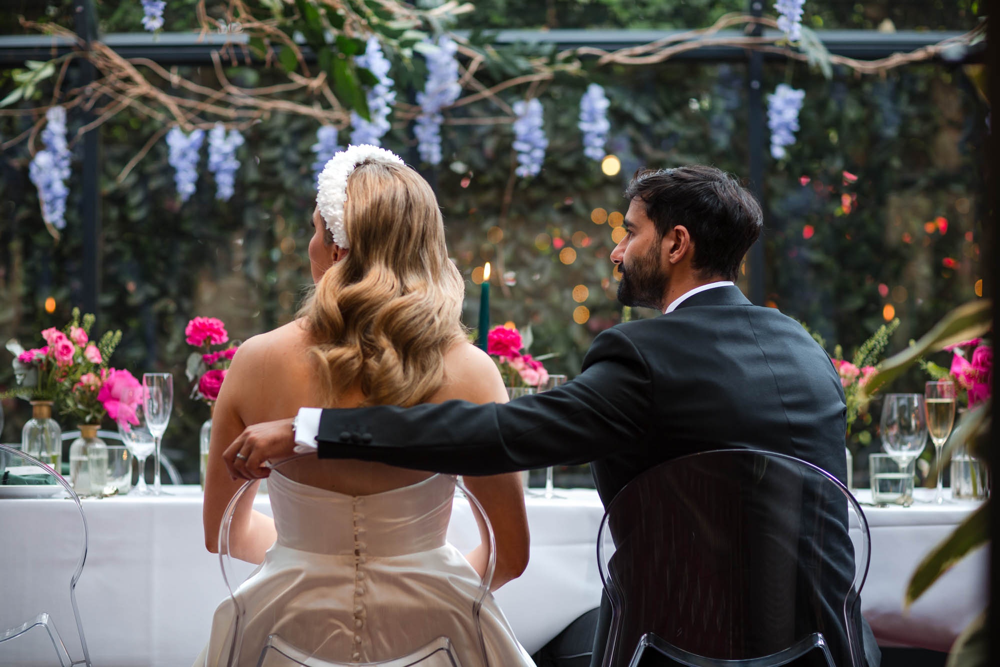 The couple seated at the head table beneath hanging wisteria, The Greenhouses