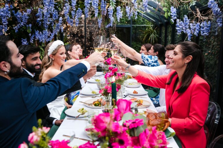 A toast raised across a table of hot pink flowers, The Greenhouses