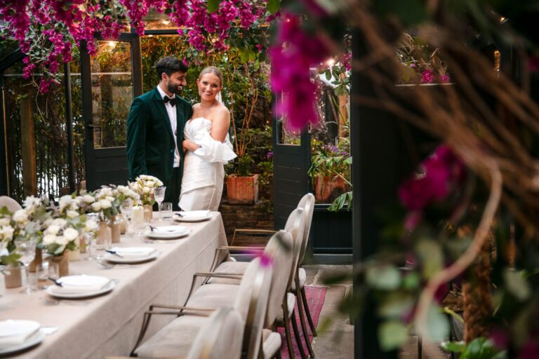 The couple framed by bougainvillea beside the dressed table, The Greenhouses