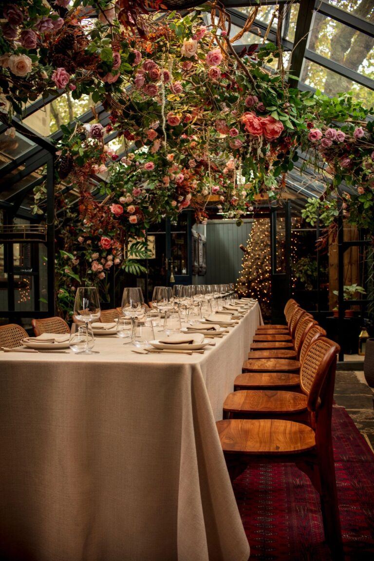 The glasshouse dressed in red and pink blossom above a laid table, The Greenhouses