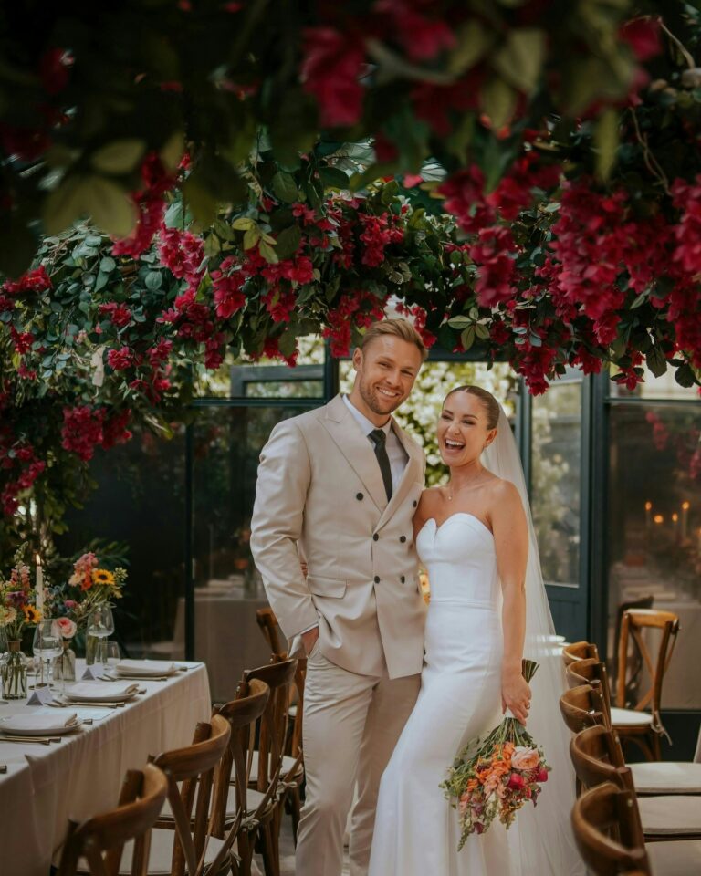 The couple beneath a crimson blossom canopy, The Greenhouses