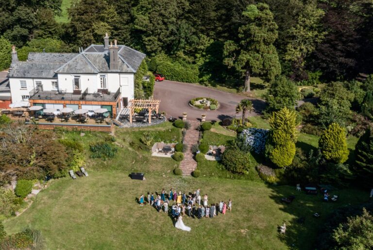 Drone view over the Main House and gardens with a wedding party gathered on the lawn for a group photograph, The Horn Of Plenty