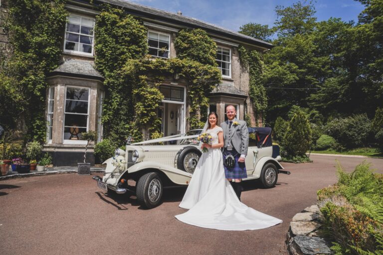 A couple beside a vintage wedding car in front of the ivy-covered Main House, The Horn Of Plenty