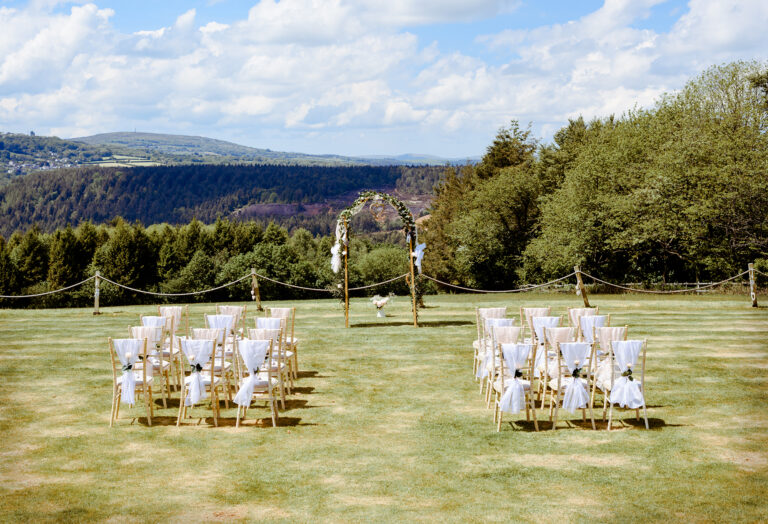 Chairs set out on the lower lawn for an outdoor ceremony, with a floral arch and the valley beyond, The Horn Of Plenty