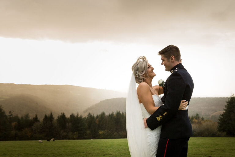 A couple on the lawn under a hazy sky, with the wooded Tamar Valley behind them, The Horn Of Plenty