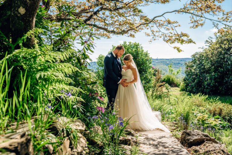 A couple among ferns and bluebells on a garden path, with the valley visible through the trees, The Horn Of Plenty