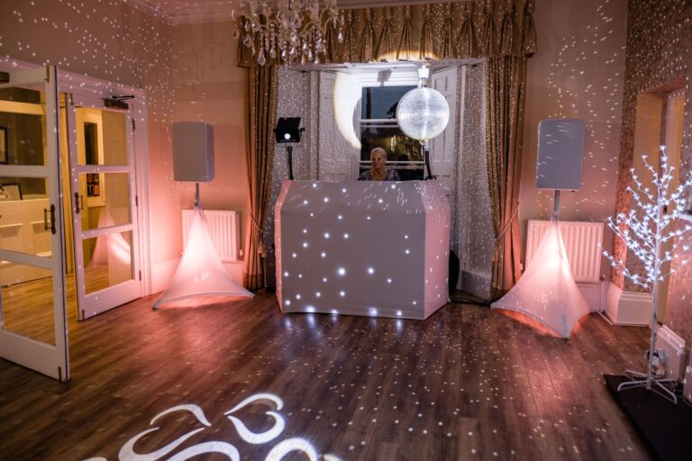 The evening room set for dancing, with a starlit DJ booth, uplighters and a lit monogram on the floor, The Horn Of Plenty