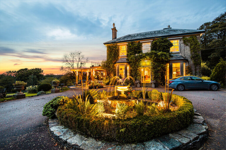 The Main House lit up at dusk, with the fountain and planted turning circle in front, The Horn Of Plenty