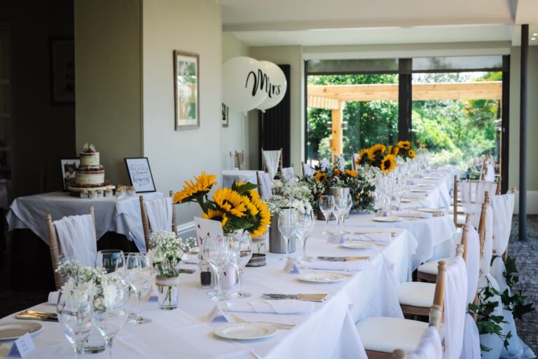 A long wedding table dressed with sunflowers, with the cake and a balloon by the windows to the terrace, The Horn Of Plenty