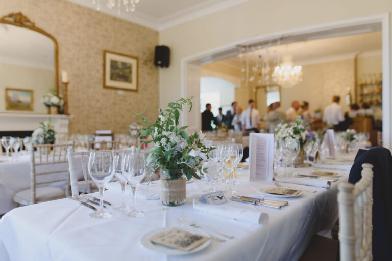 A Main House room set with long tables, glassware and jar flowers, opening through to the bar, The Horn Of Plenty