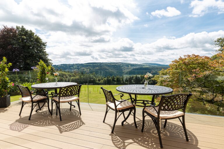 The decked terrace outside the restaurant, with glass balustrades and wrought-iron tables above the lawn, The Horn Of Plenty