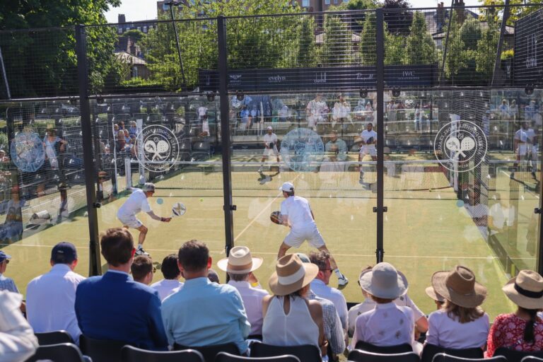 Players on a glass padel court before a seated crowd at a summer classic, The Hurlingham Club