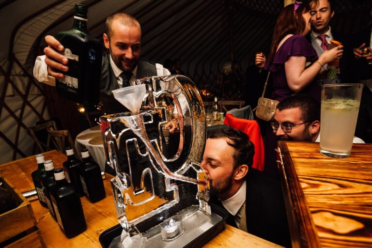 An ice letter carved as a cocktail pour, with bartenders and guests around it, The Ice Box