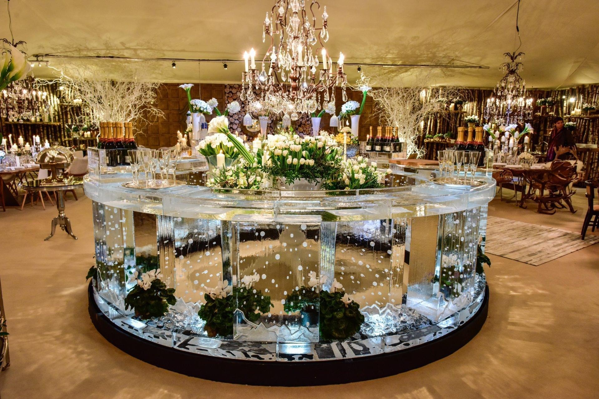 A 4m circular ice bar dressed with flowers and greenery under a chandelier, for a private wedding, The Ice Box