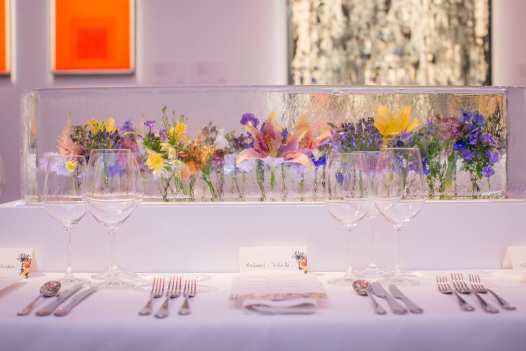 A long block of ice holding fresh spring flowers along a dinner table set for a formal gallery dinner, London, The Ice Box