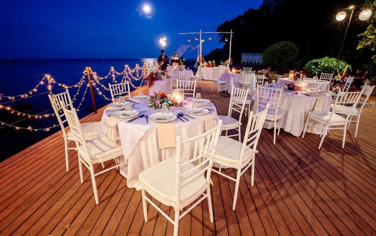 Round tables dressed for a wedding dinner on the deck at dusk, The Kala Samui