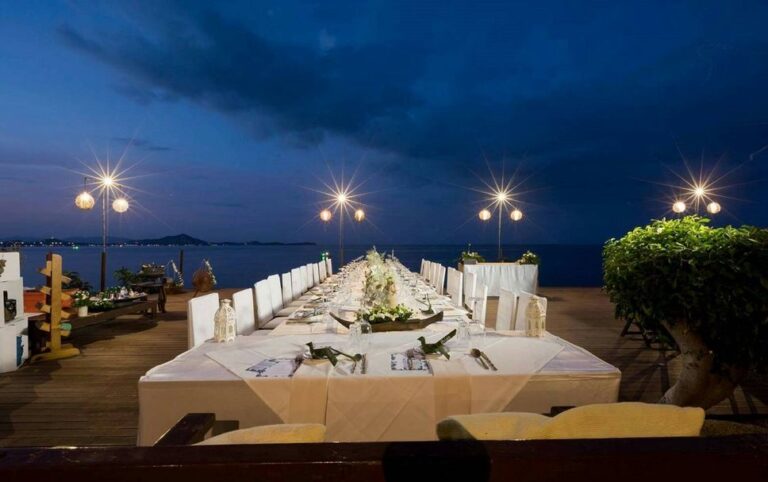 Long banquet table set on the deck at night beside the sea, The Kala Samui