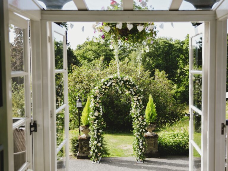 A floral ceremony arch through open French doors to the garden, The Lake Country House Hotel & Spa