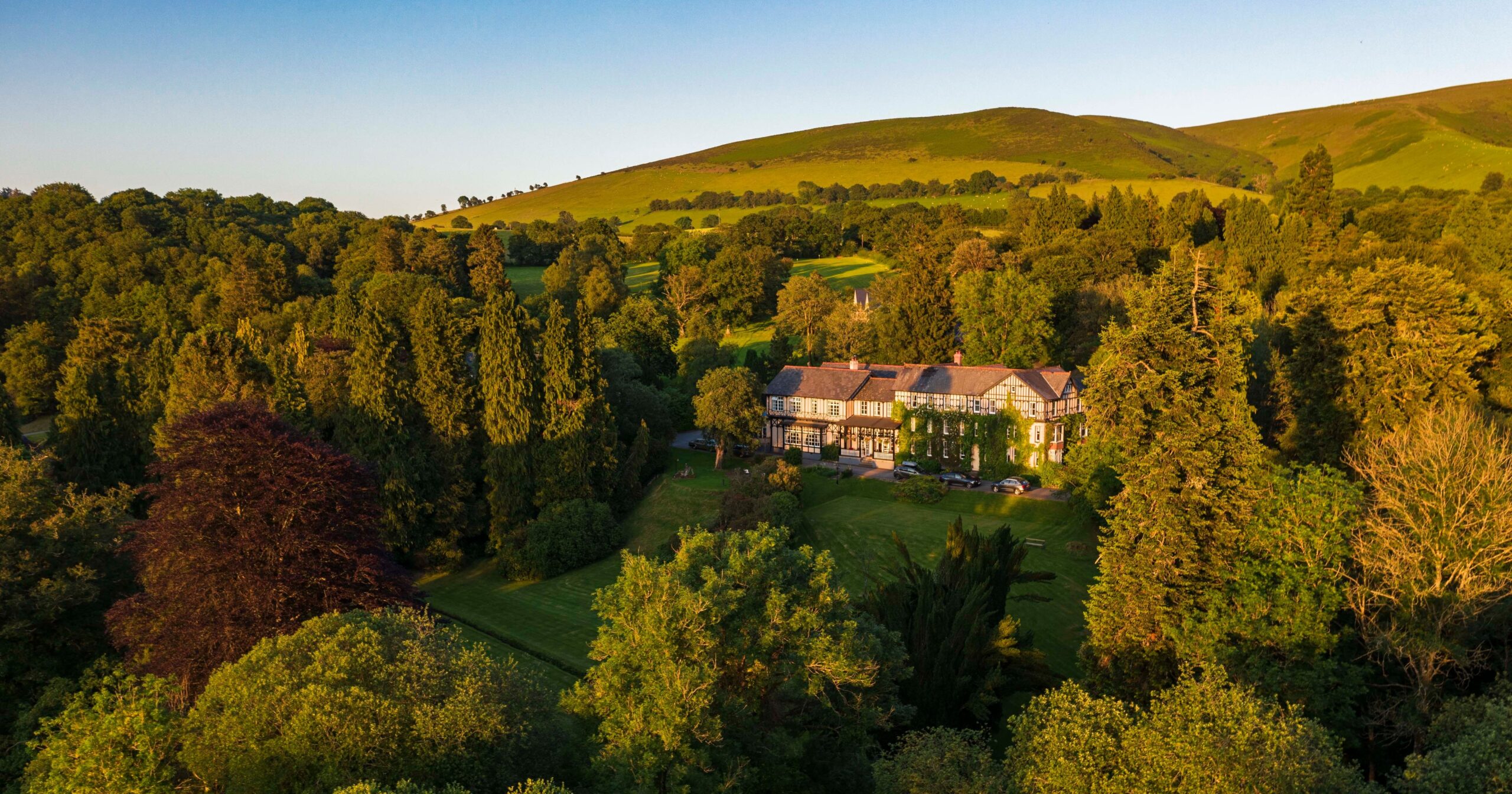 Golden-hour aerial: the house in 50 acres of woodland and hills, The Lake Country House Hotel & Spa