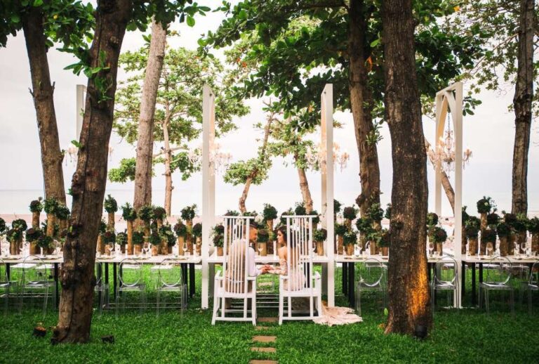 Garden ceremony set-up under tall trees with flower arrangements, The Library