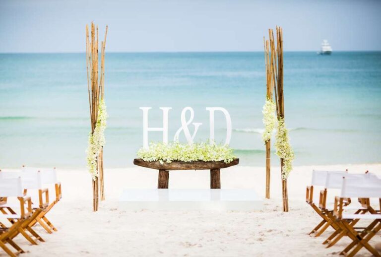 Beach ceremony arch with an initials sign and wooden folding chairs, The Library