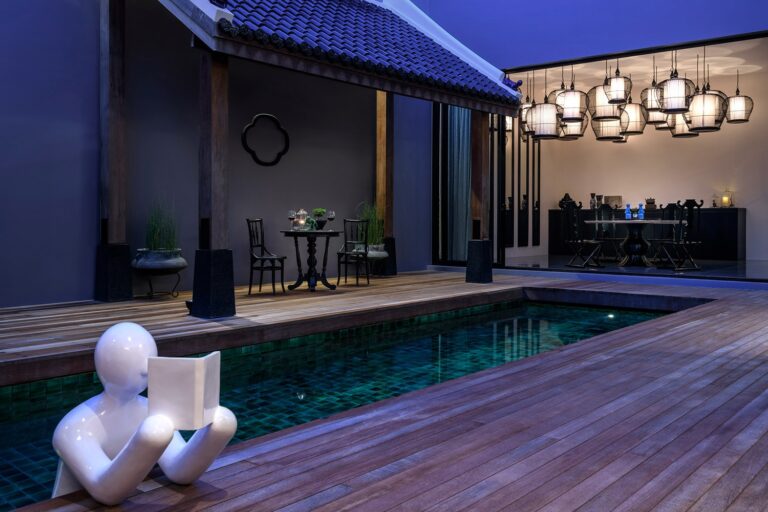 Private pool, deck and lantern-lit dining pavilion at The Editor villa at dusk, The Library