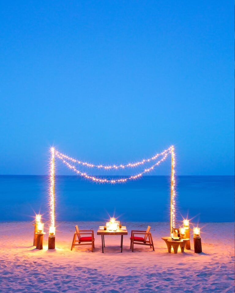 Dinner for two on the sand under strings of lights at dusk, The Library