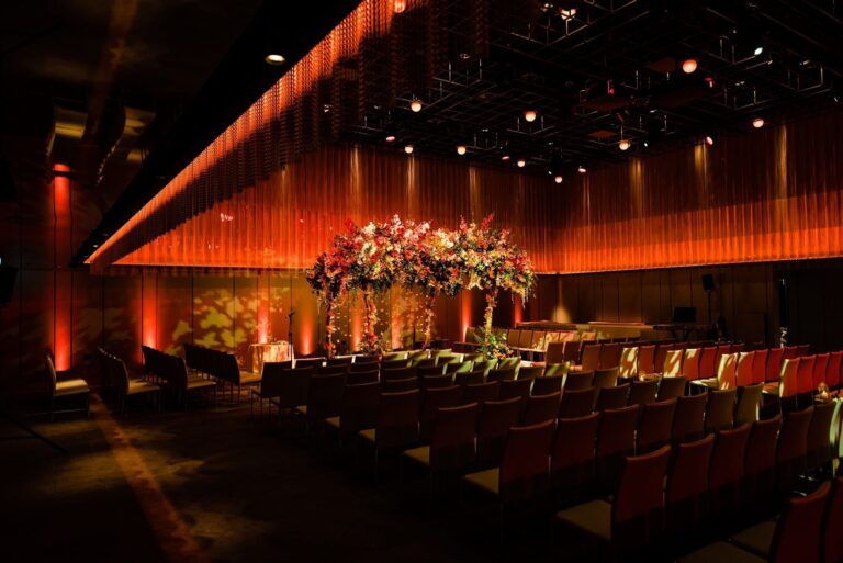 Rows of chairs facing a floral canopy in the Ballroom, lit in amber, The Londoner