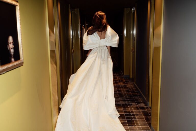 A bride walking away down a hotel corridor in a gown with a large bow and train, The Londoner
