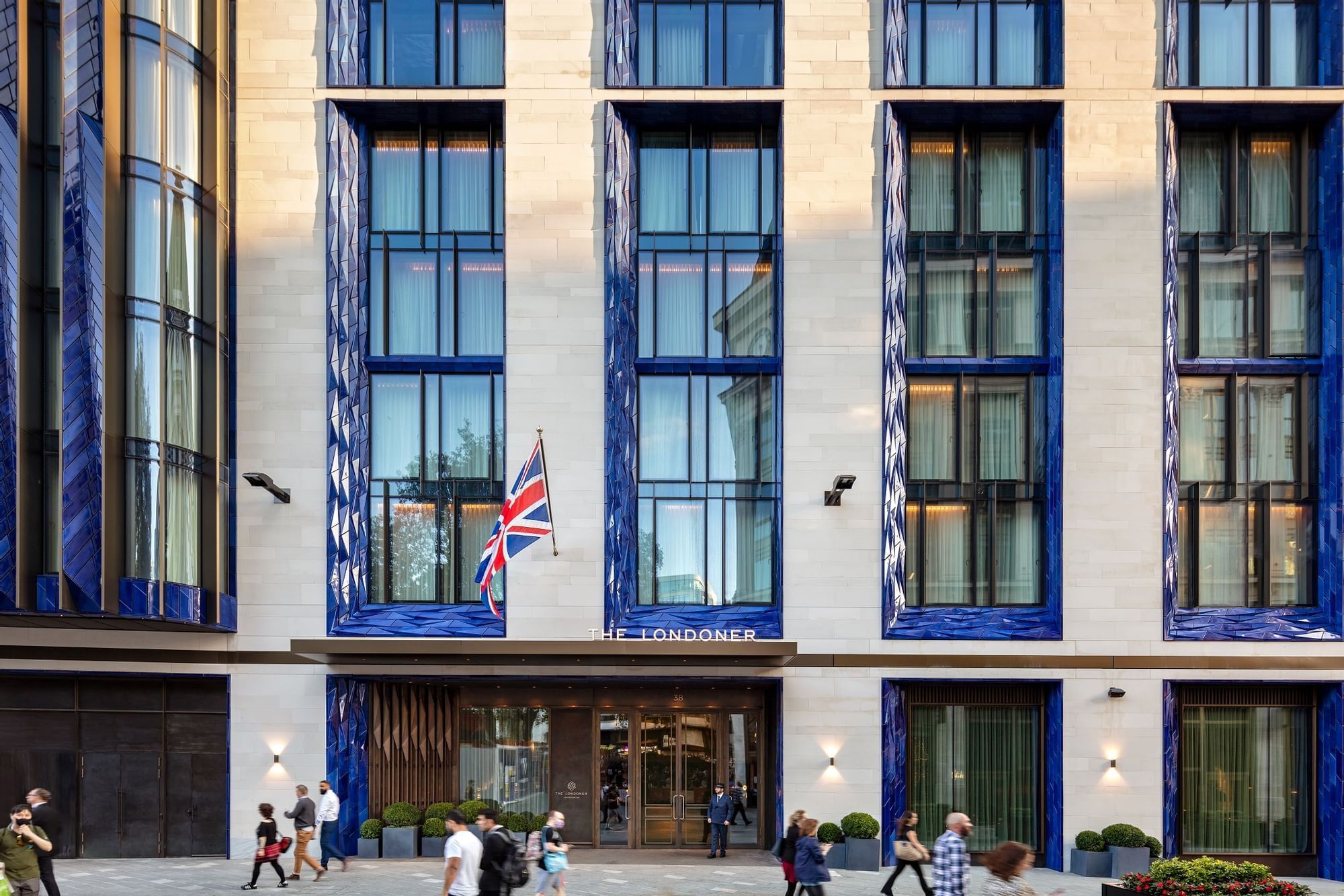 The stone and blue-glazed facade of The Londoner on Leicester Square, with the main entrance and Union flag at street level, The Londoner