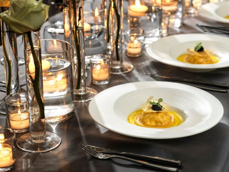 Plated ravioli in a golden sauce topped with caviar, on a candlelit table, The Londoner
