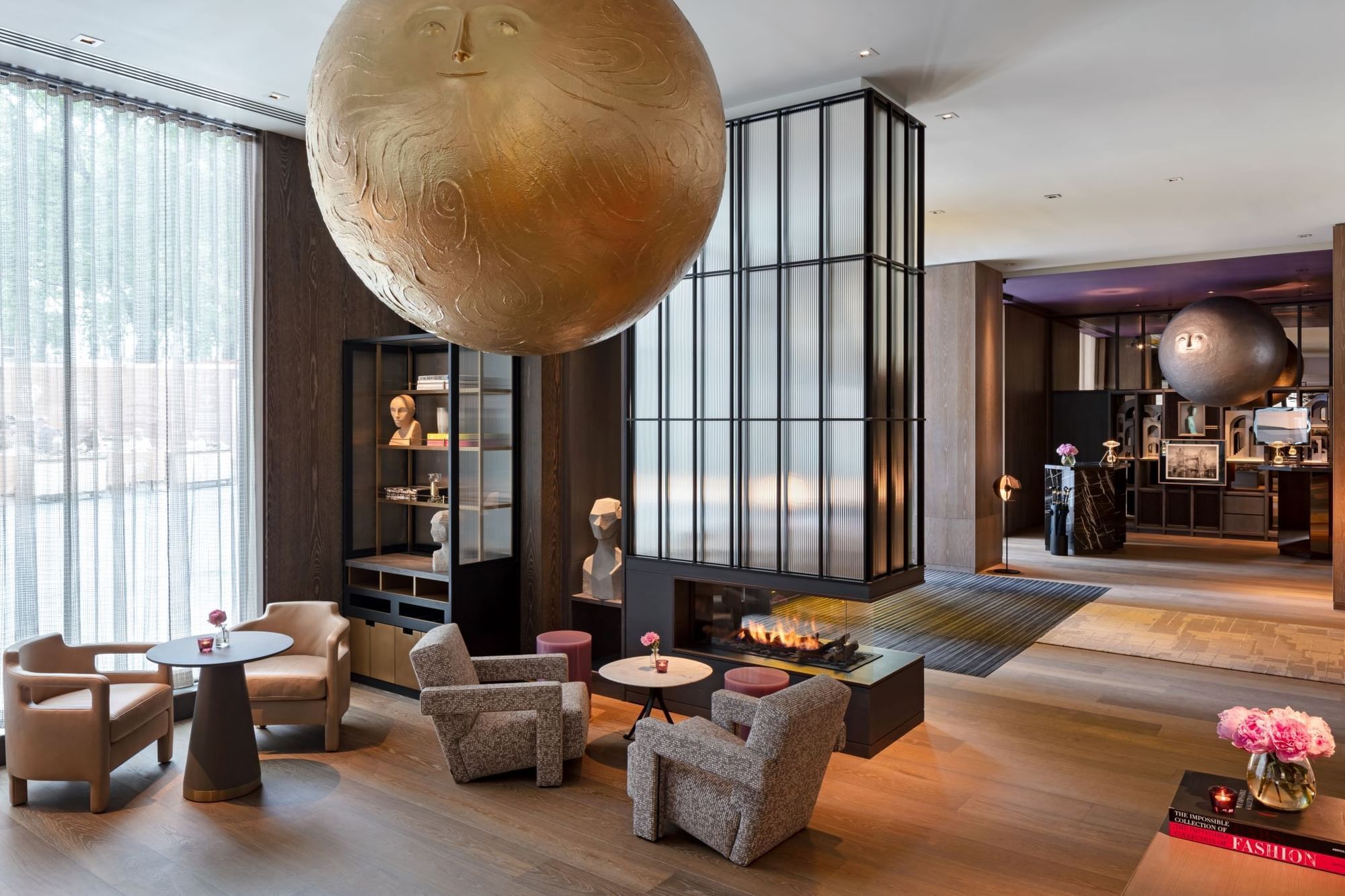 The lobby lounge, with armchairs around a fireplace under a large gilded sphere, The Londoner