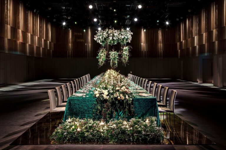 A single long table with green cloths and banks of white flowers in the middle of the Ballroom, The Londoner