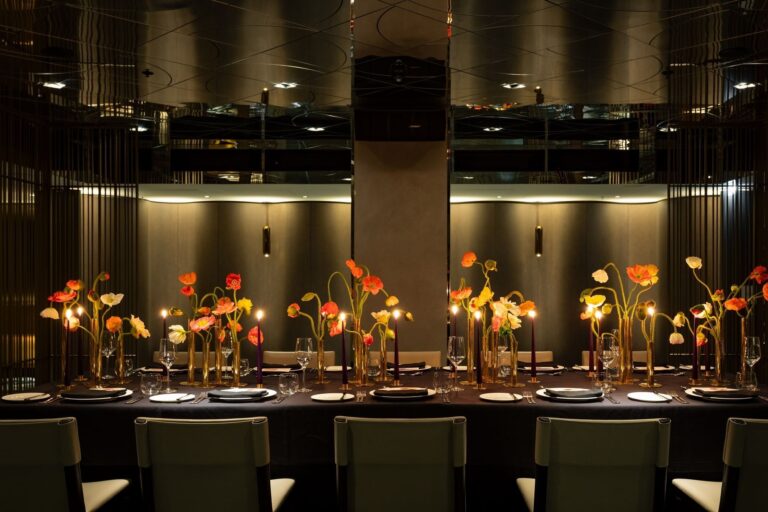 A long table in the Green Room set for dinner, with poppies in brass vases and the bar behind, The Londoner