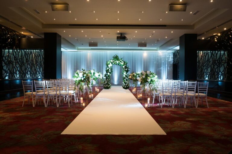 The Danziger Suite laid out for a ceremony, with a white aisle, rows of white chairs and a floral arch, The May Fair