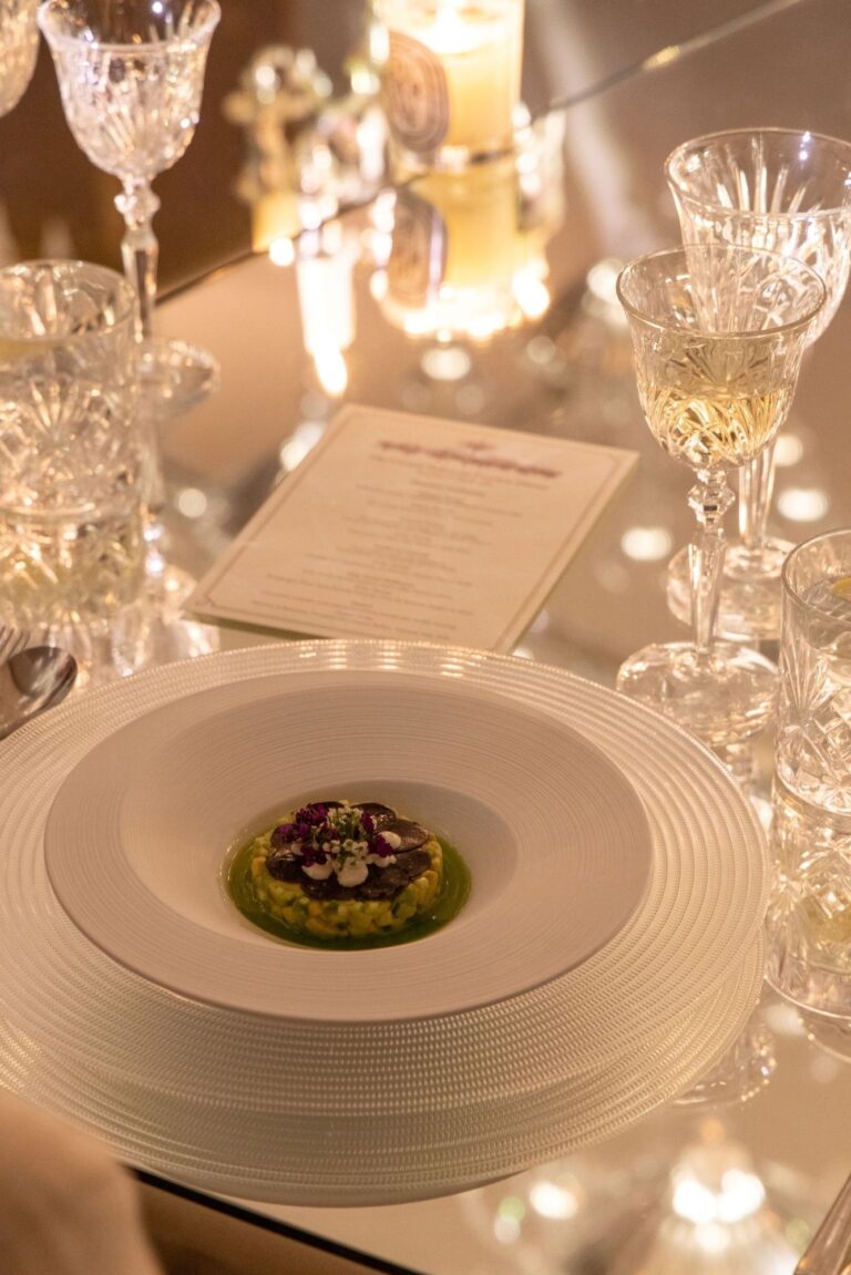 A dinner place setting in the Crystal Ballroom with a printed menu, cut-glass crystal and a plated starter, The May Fair