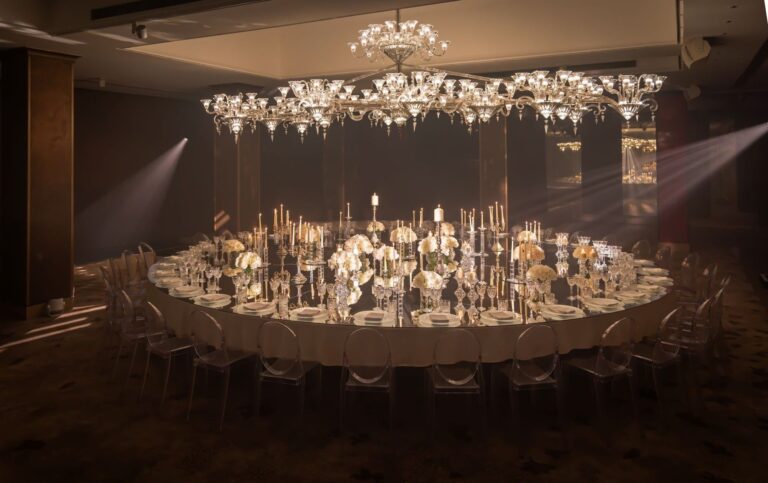 A single large round table dressed with white flowers and candelabra beneath the Crystal Ballroom chandeliers, The May Fair
