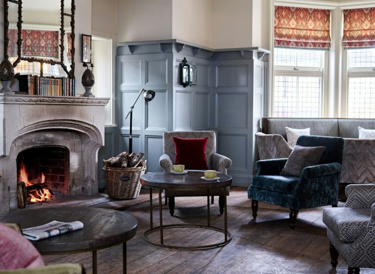 The drawing room, the carved stone fireplace lit, armchairs and a leaded bay window, The Montagu Arms Hotel