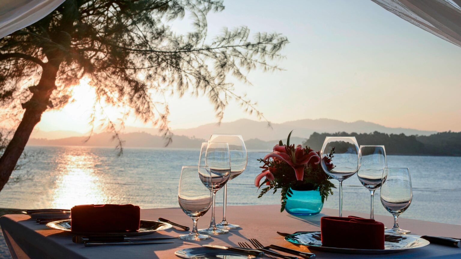 A private dining table set beside the sea at sunset
