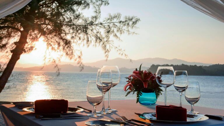 Private dining table set beside the sea at sunset, The Naka Island, A Luxury Collection Resort and Spa, Phuket