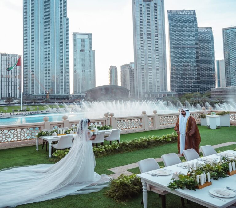 A bride beside a long garden table on the lawn, with the fountain behind, The Palace Downtown Dubai