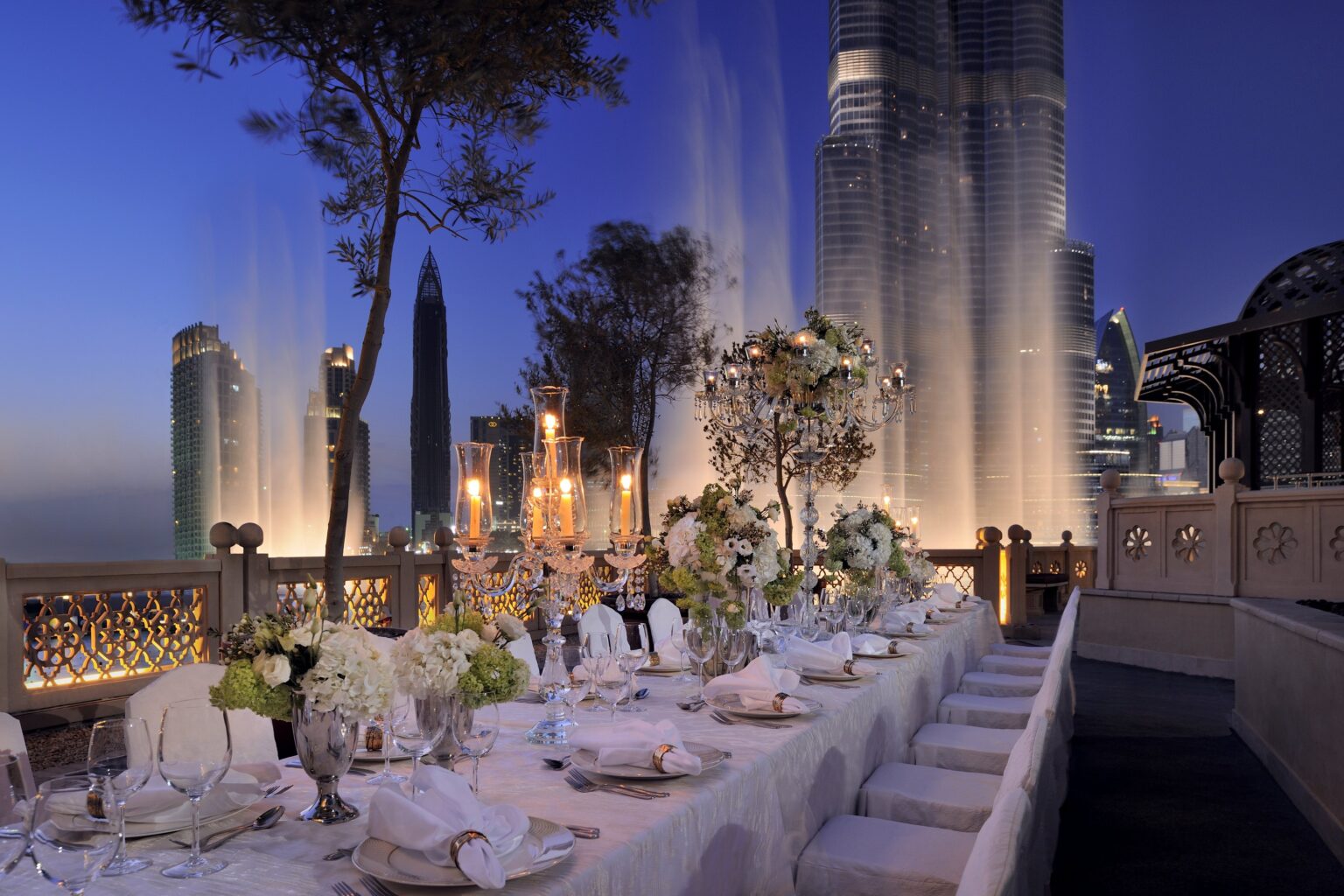 A long wedding dinner table on the Viewing Deck at dusk with the Dubai Fountain beyond, The Palace Downtown