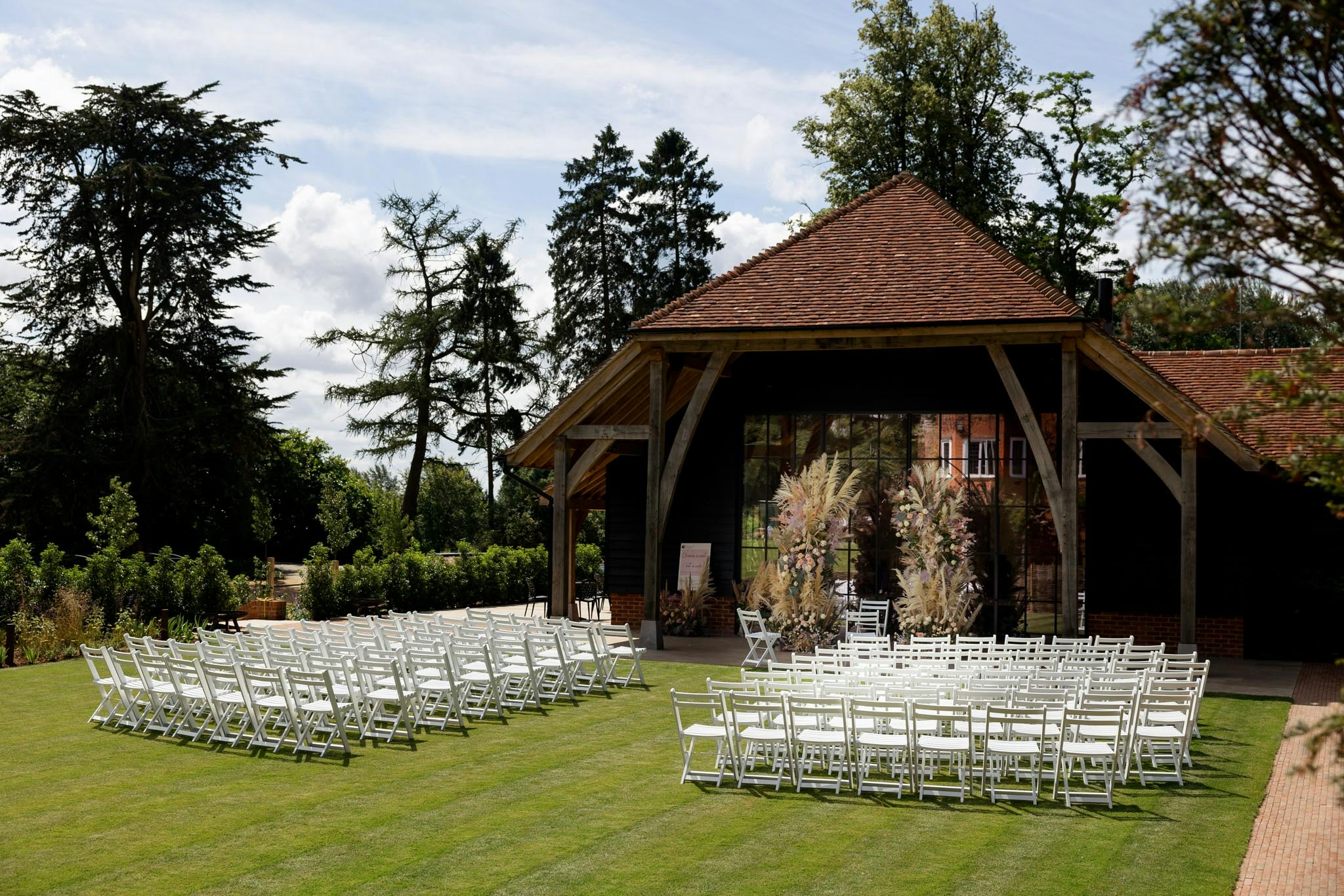The lawn set for an outdoor ceremony beside the barn, with tall conifers and cedars behind, The Post Barn